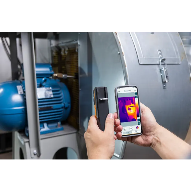 Person using a smartphone with thermal imaging app on a machine.