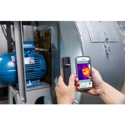 Person using a smartphone with thermal imaging app on a machine.
