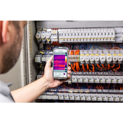 Person using a smartphone with thermal imaging app on electrical panel