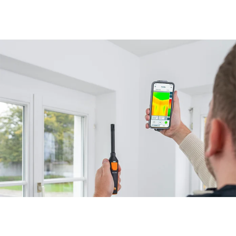 Person using a thermal imaging device and smartphone to check temperature inside a room.