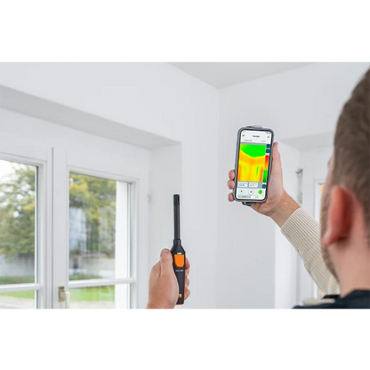 Person using a thermal imaging device and smartphone to check temperature inside a room.