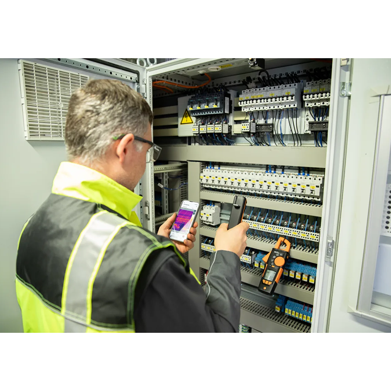 Person in safety vest using a device in front of an electrical panel.